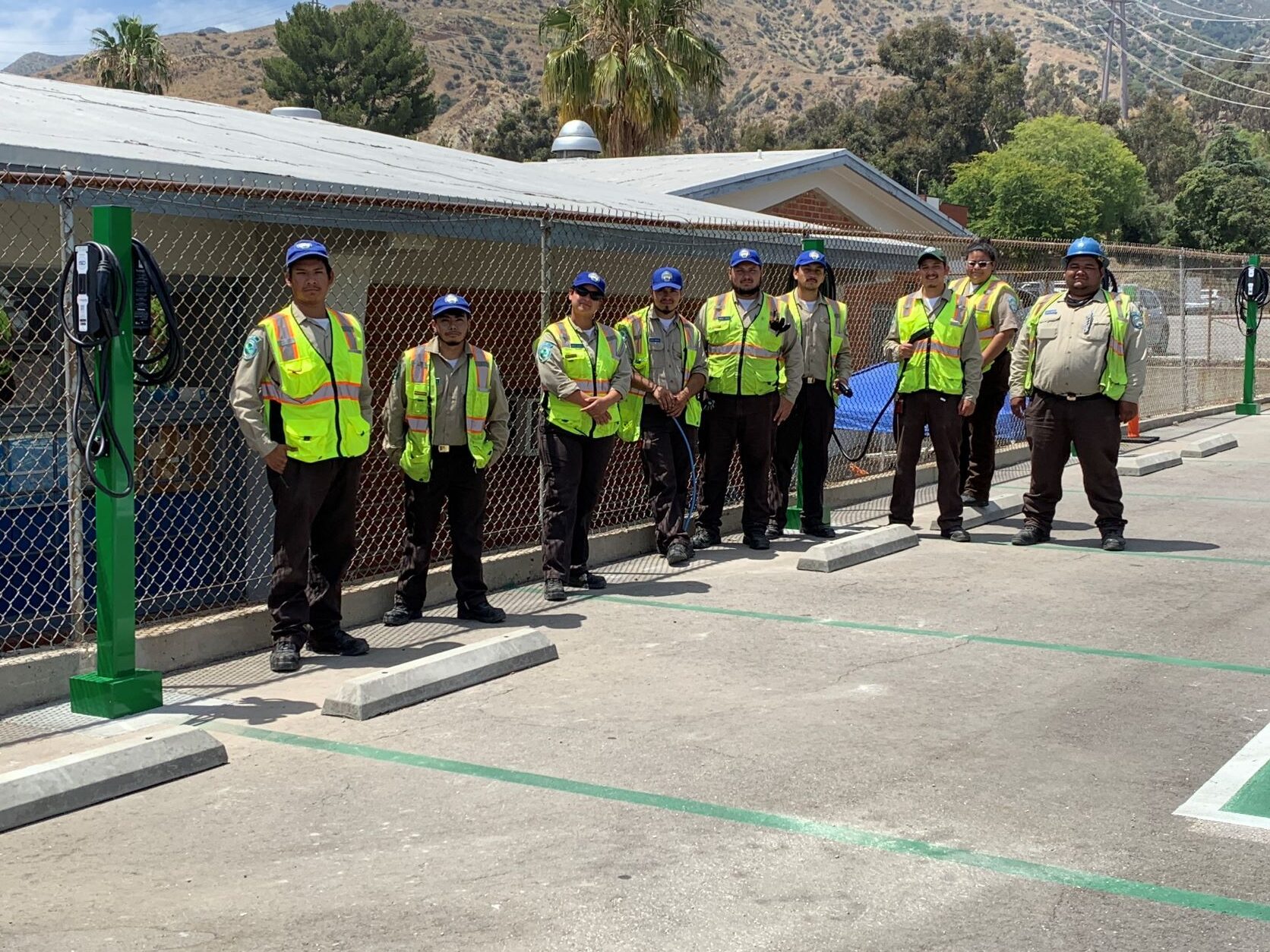 A group of workers in safety vests stands by electric vehicle charging stations in a clean transportation facility.