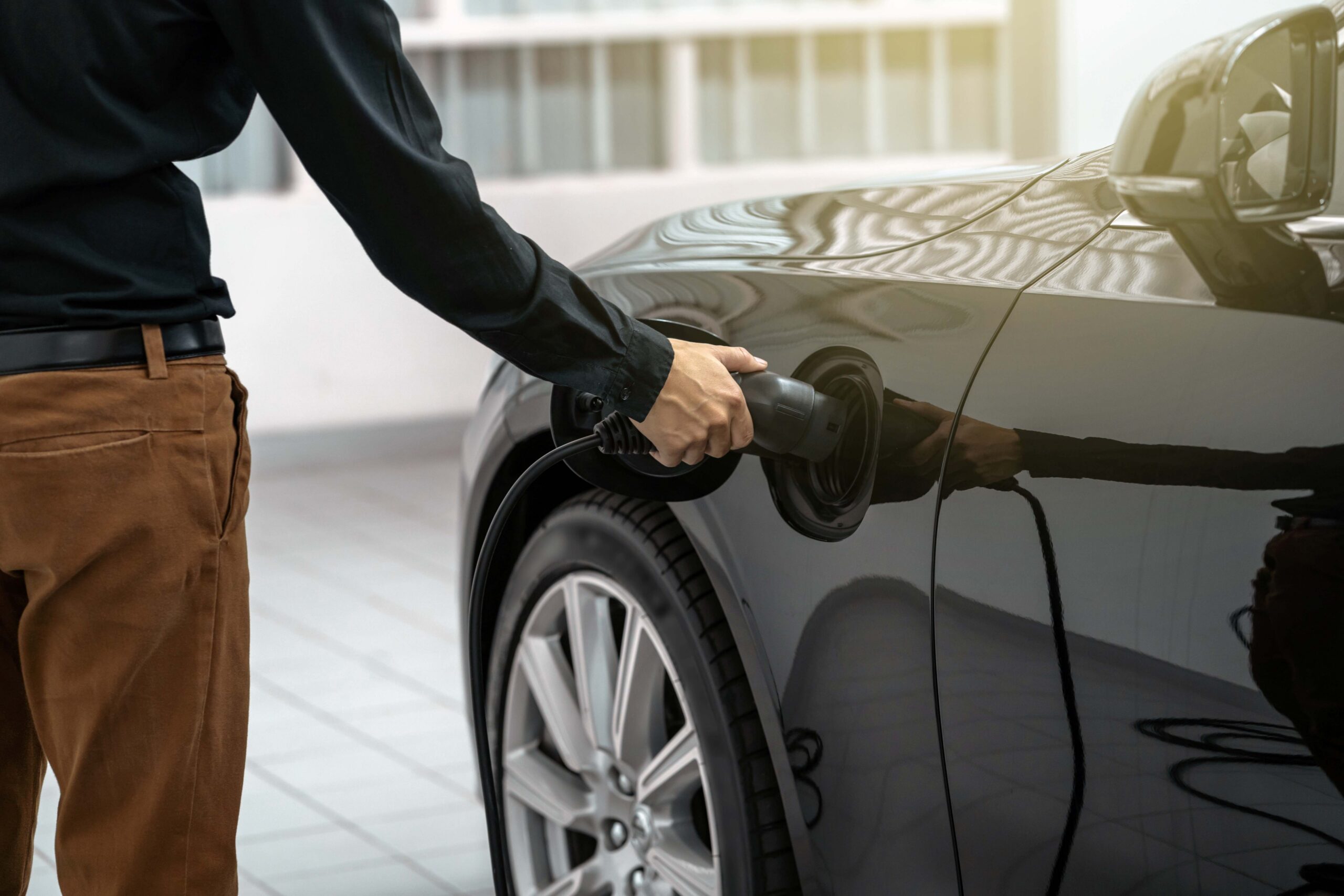 A person connects a charging cable to an electric vehicle in a bright, modern setting.
