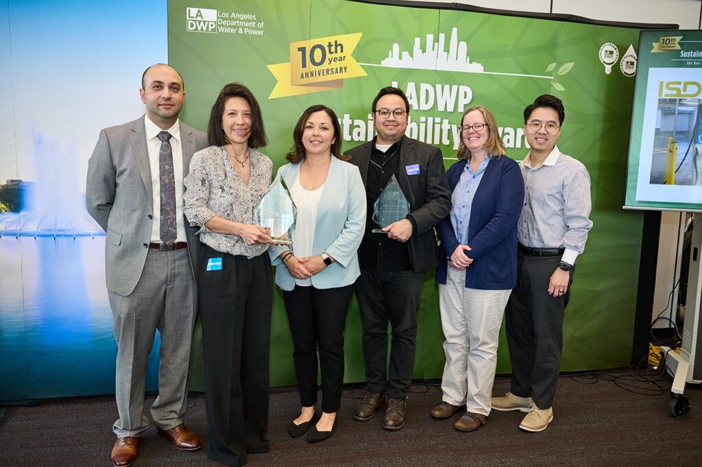 A group of six people from the Los Angeles County Internal Services Department stand together holding glass awards at the LADWP Sustainability Awards 10th Anniversary event. A banner behind them reads &ldquo;LADWP Sustainability Awards&rdquo; with the Los Angeles Department of Water and Power logo.