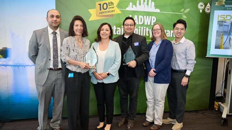 A group of six people from the Los Angeles County Internal Services Department stand together holding glass awards at the LADWP Sustainability Awards 10th Anniversary event. A banner behind them reads &ldquo;LADWP Sustainability Awards&rdquo; with the Los Angeles Department of Water and Power logo.