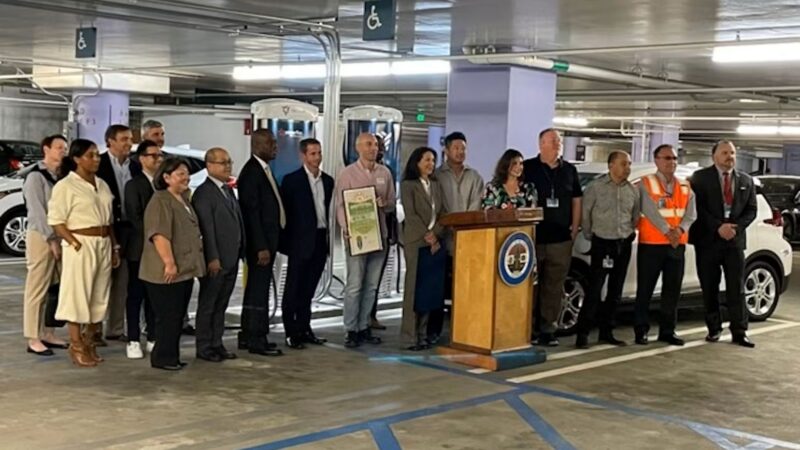 Officials and community members gather at a podium to discuss clean transportation initiatives in a parking garage.