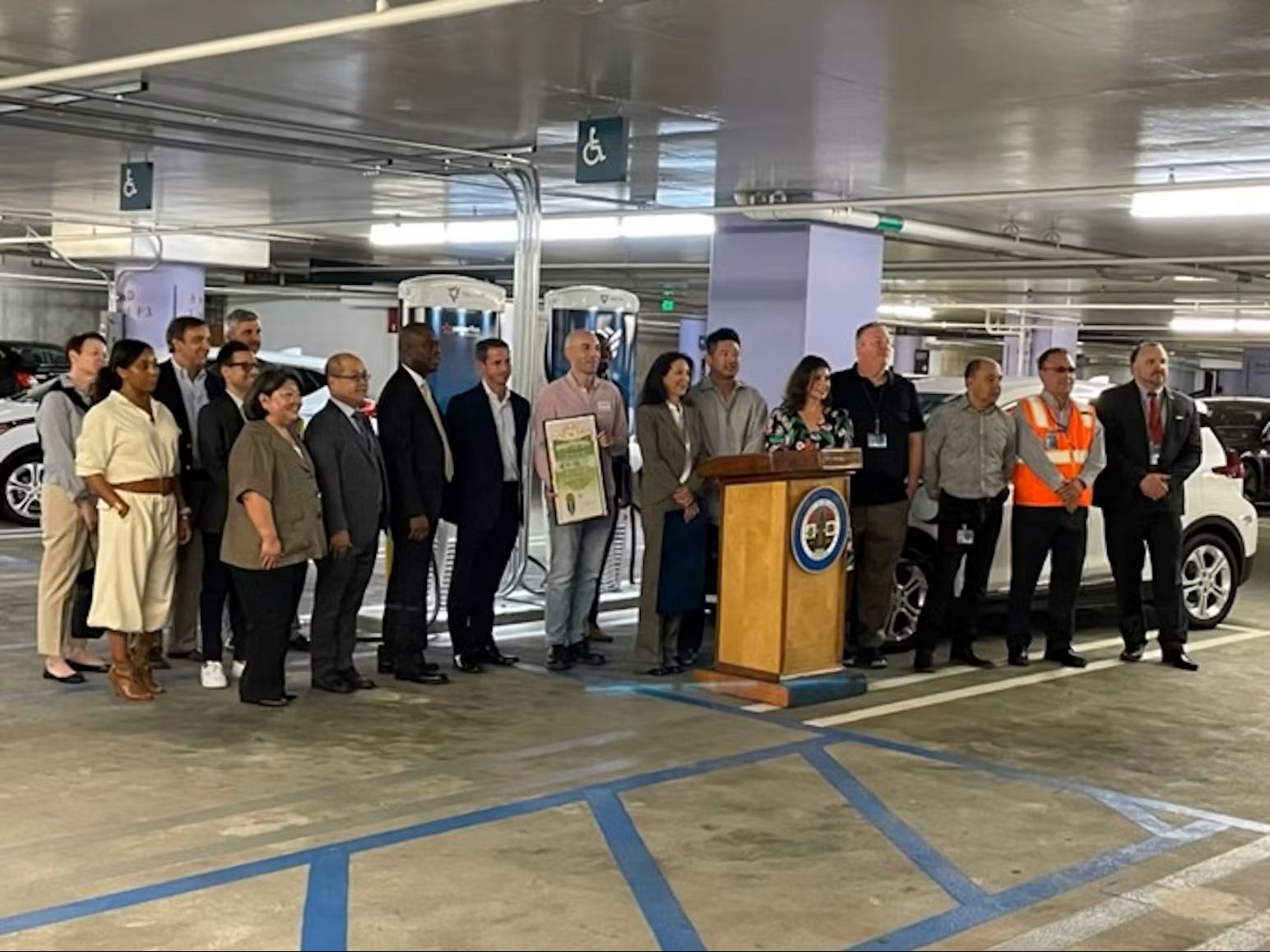 Officials and community members gather at a podium to discuss clean transportation initiatives in a parking garage.