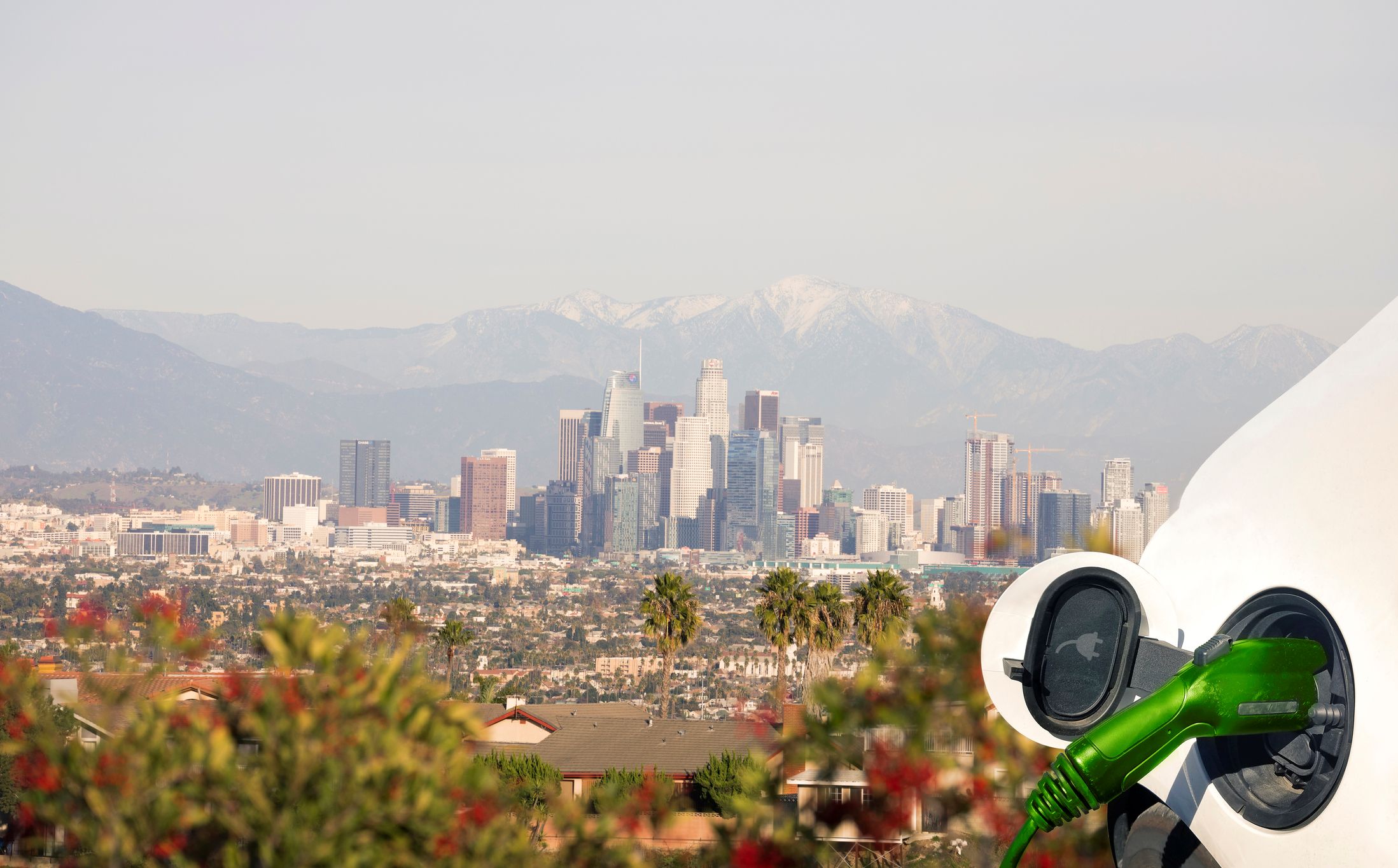 A close-up of an electric vehicle charging station with the Los Angeles skyline and mountains in the background.