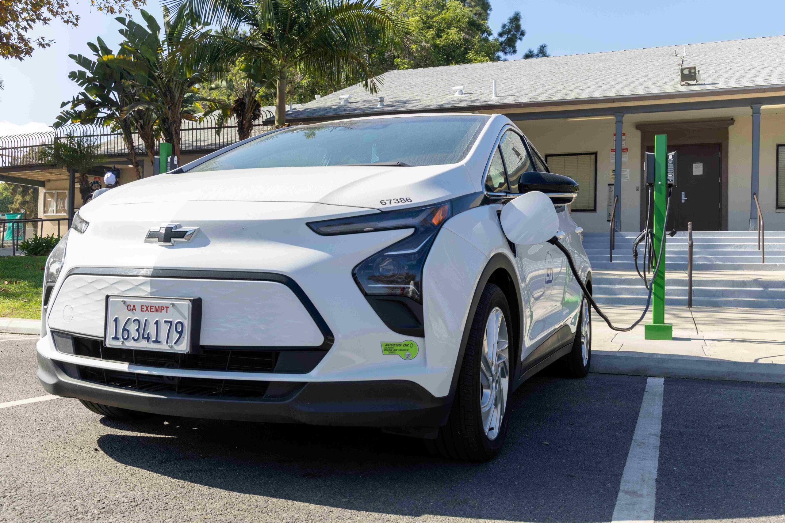 A white electric vehicle charging at a station in a community setting, promoting clean transportation initiatives.